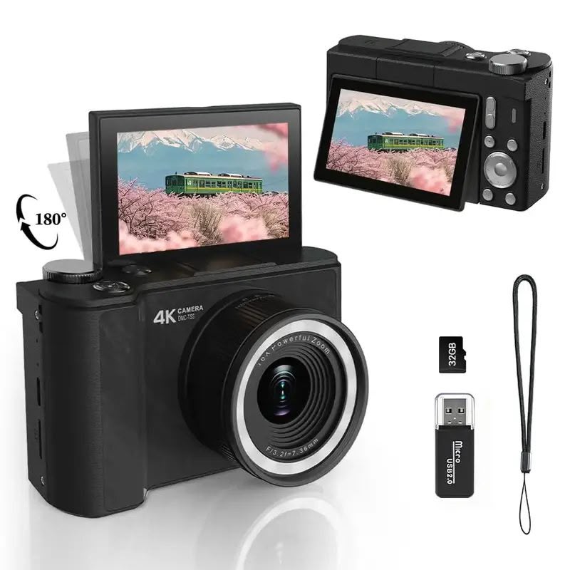 Black compact mirrorless camera with a 180-degree flip-out screen, shown with a lens, USB flash, memory card, and wrist strap on a white background.
